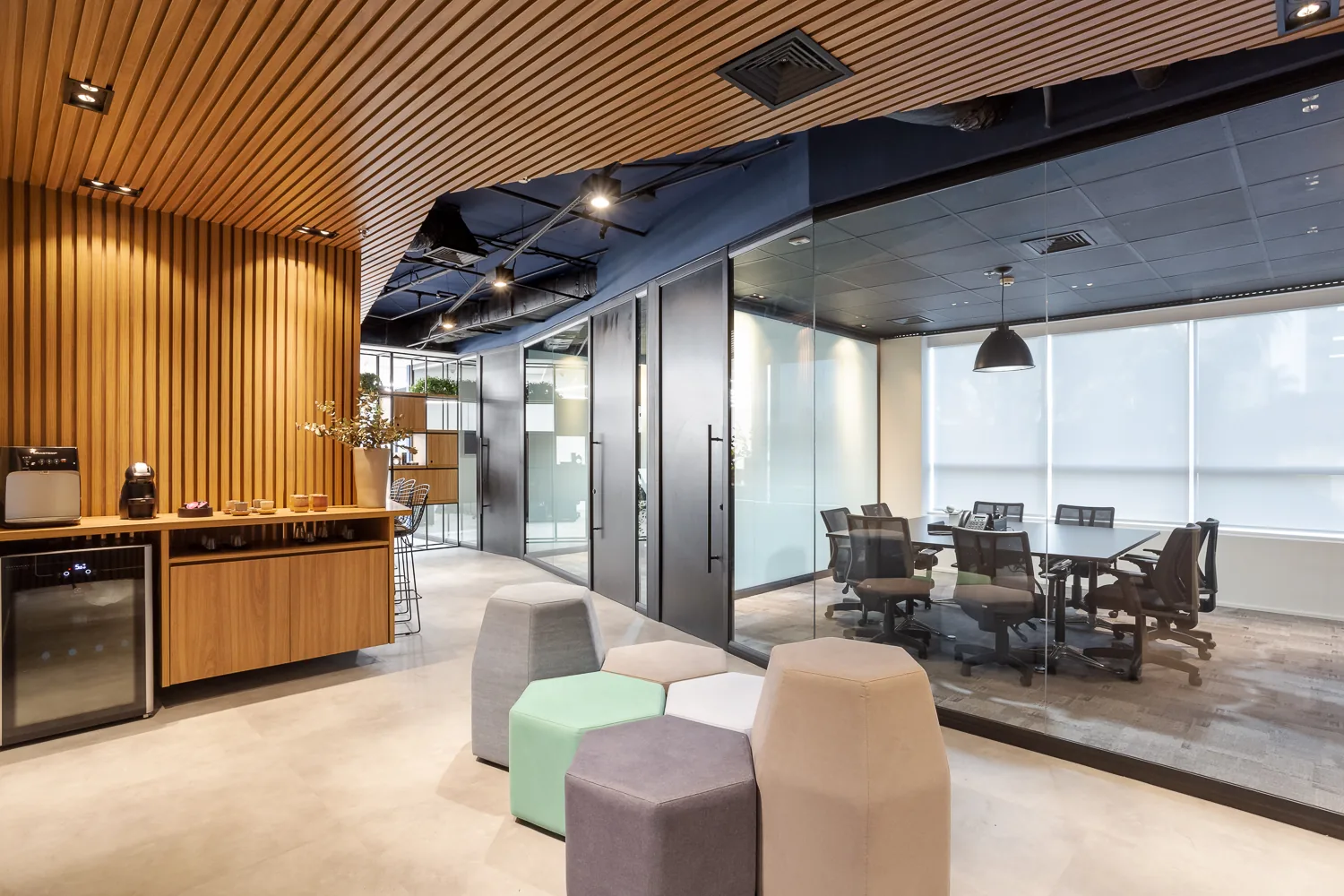 Recepção de escritório corporativo entregue pela Agyle, com parede ripada em madeira, sala de reunião de vidro e lounge com pufes